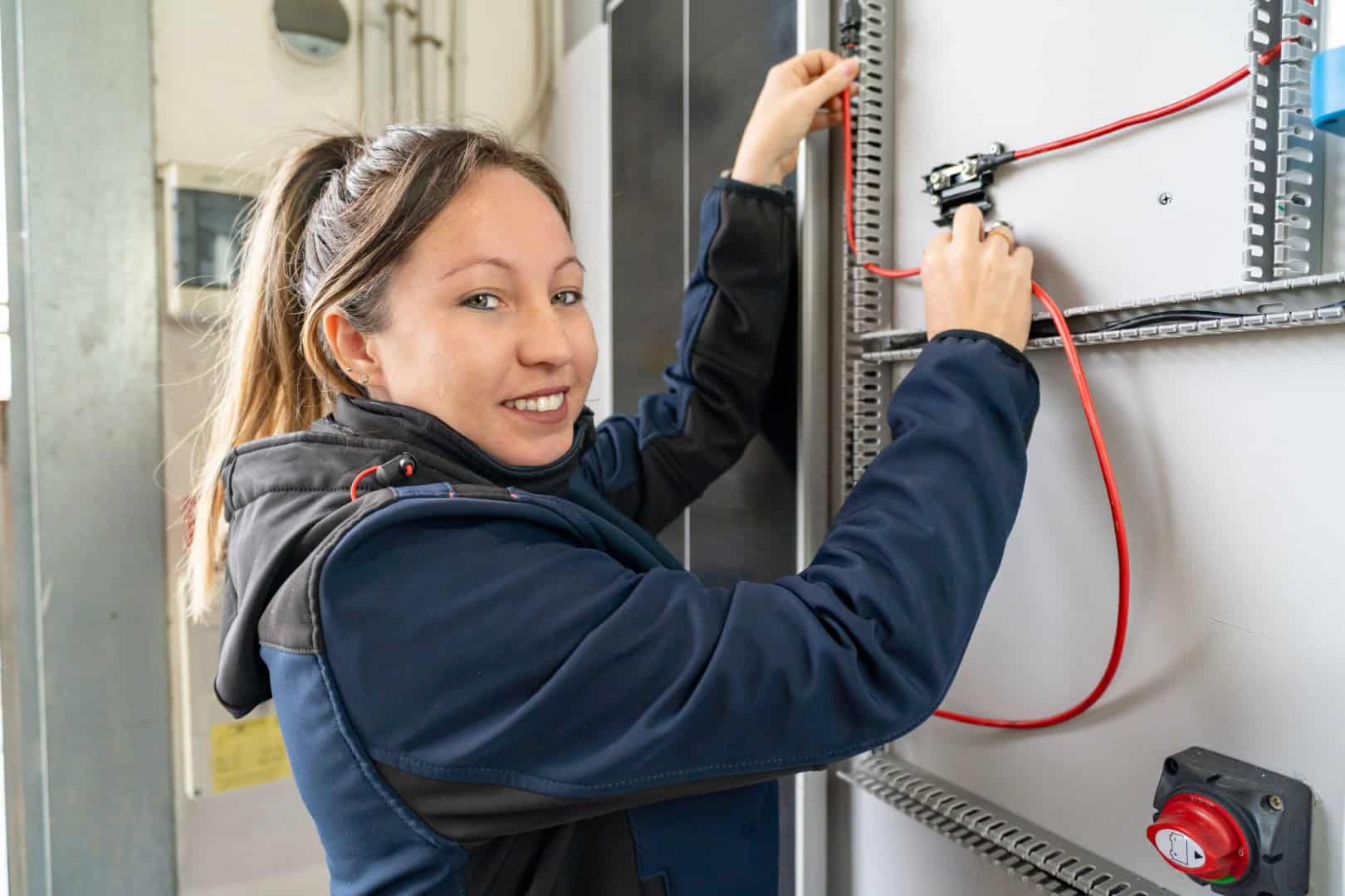 Woman technician working on an electrical switchboard, connecting red wires and smiling